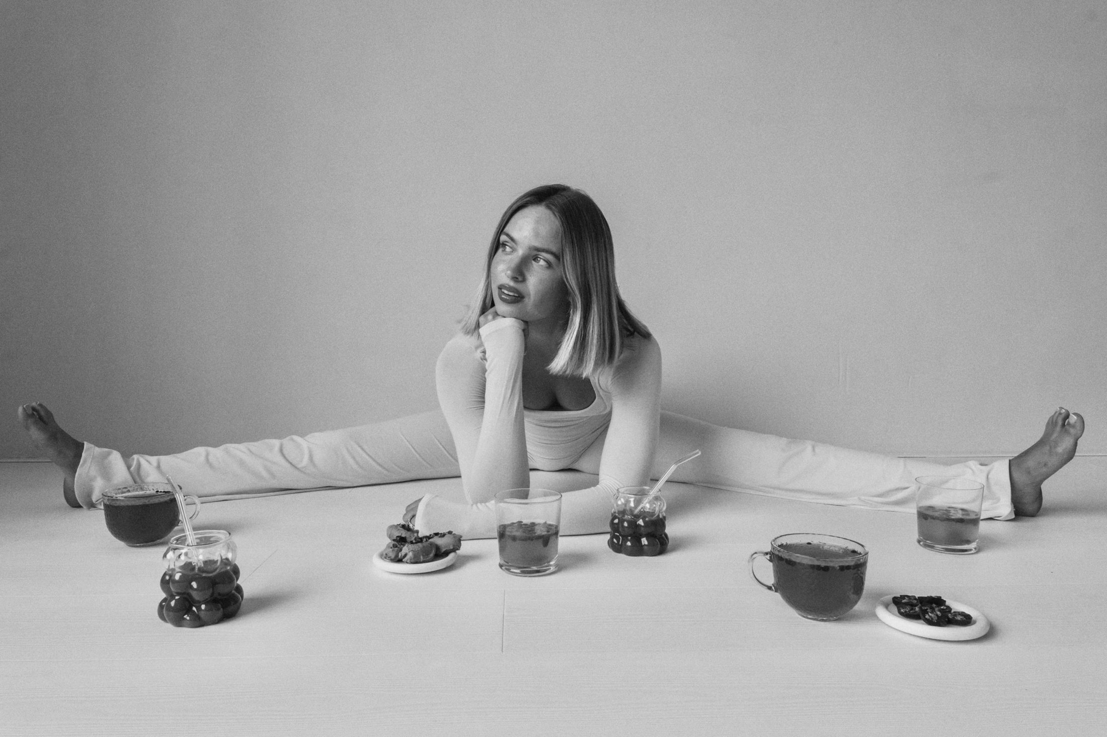 Ninalotte sitting on the floor in a split, surrounded by glasses of tea and berry drinks