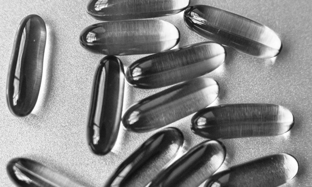 Clear fish oil capsules on a silver surface, black and white